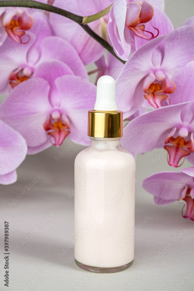 Pink anti-aging collagen, facial serum in transparent glass bottle with gold pipette and natural orchid flower on grey background. Natural Organic Spa Cosmetic Beauty Concept. Front view Pink anti-aging collagen, facial serum in transparent glass bottle with gold pipette and natural orchid flower on grey background. Natural Organic Spa Cosmetic Beauty Concept. Front view
