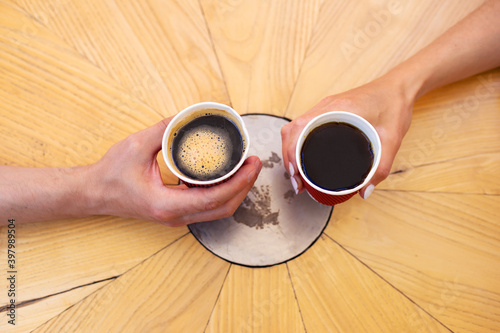 A wooden table on which there is a red plastic cup with coffee. The hands of the girl and the guy are holding a glass of coffee.