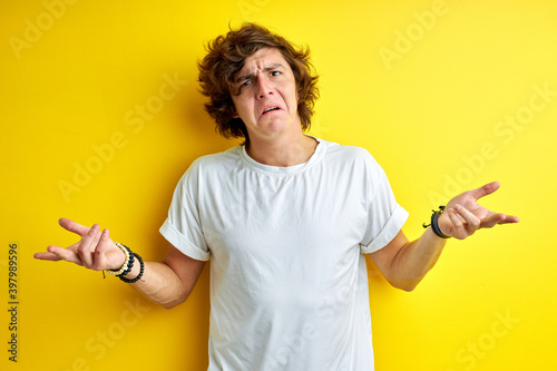 guy has a question. misunderstanding man shrugging at camera isolated on yellow background, spreading arms, confused photo