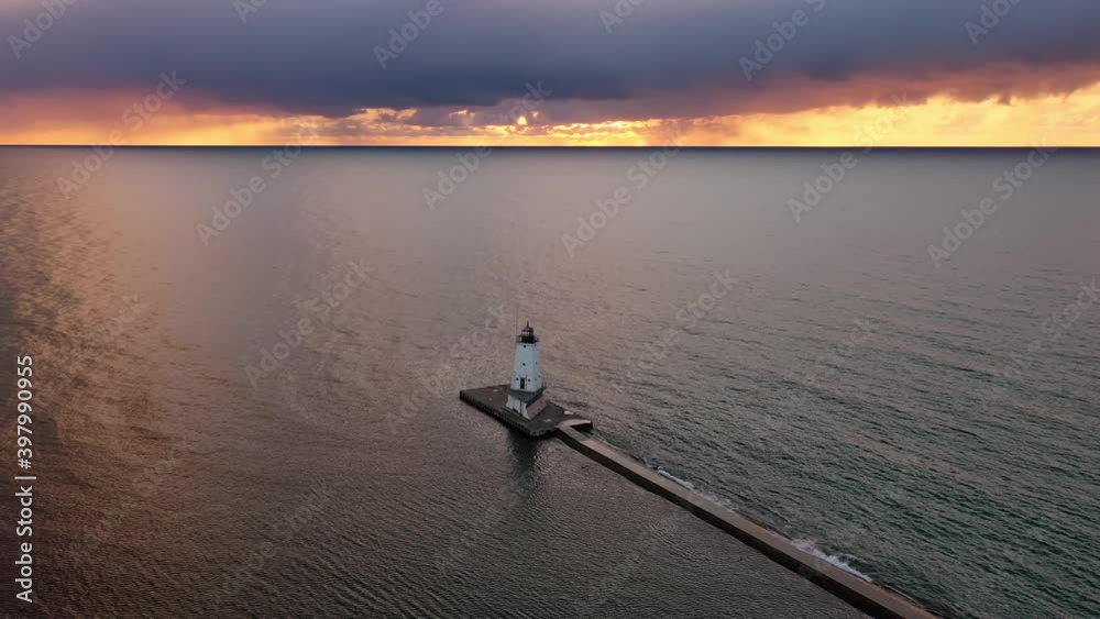 Beautiful sunset aerial rising high up above the white colored Ludington breakwater lighthouse with blue and orange sky and clouds above reflecting on the calm water of Lake Michigan below. Beautiful sunset aerial rising high up above the white colored Ludington breakwater lighthouse with blue and orange sky and clouds above reflecting on the calm water of Lake Michigan below.