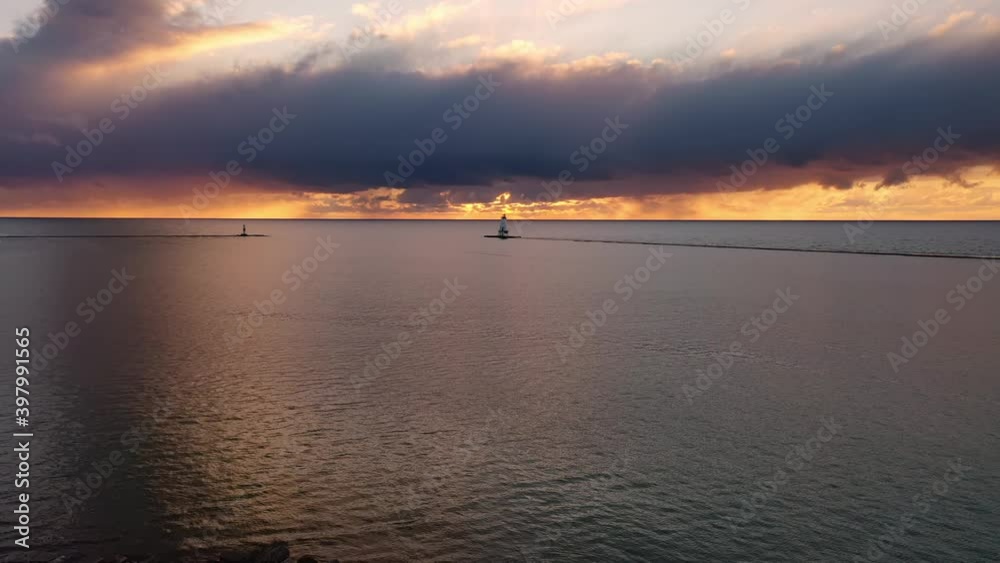 Beautiful sunset aerial panning in over a pier towards the white colored Ludington breakwater lighthouse with blue and orange sky and clouds above reflecting on the calm water of Lake Michigan. Beautiful sunset aerial panning in over a pier towards the white colored Ludington breakwater lighthouse with blue and orange sky and clouds above reflecting on the calm water of Lake Michigan.
