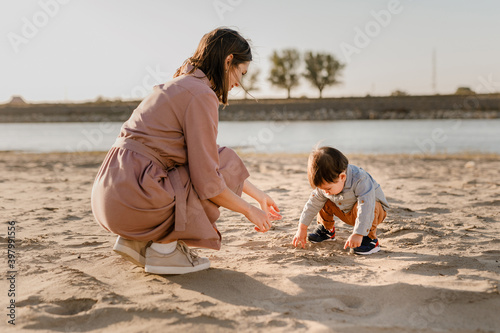 Portrait of loving mother and his one years old son walking and playing with sand