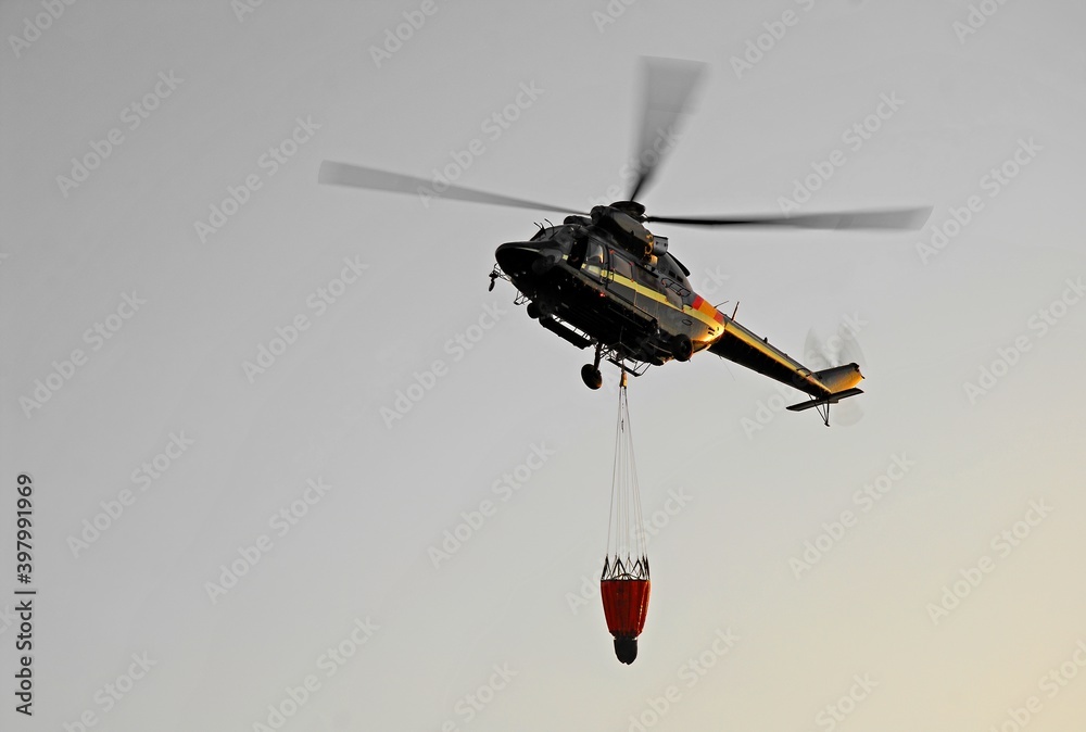 A firefighting helicopter loads a bag of water