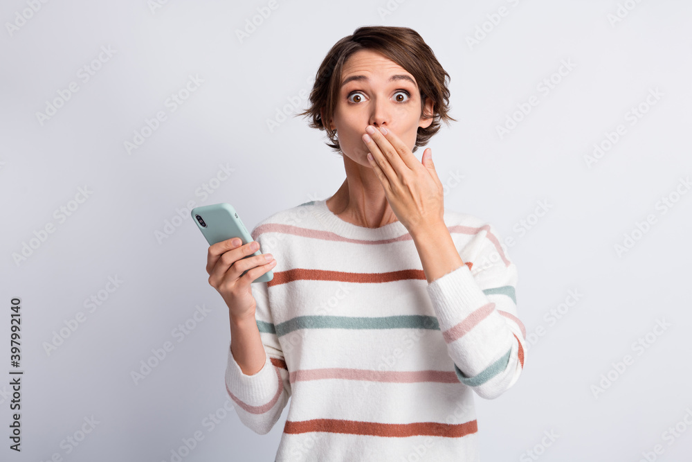 Photo of guilty young woman dressed striped pullover holding modern device arm cover mouth isolated grey color background Photo of guilty young woman dressed striped pullover holding modern device arm cover mouth isolated grey color background