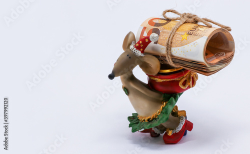 A Christmas mouse figurine holds a roll of Euro money with a face value of 50 euros. Free space. The concept of cash during the Christmas holidays. A symbol of savings, investment, and wealth.