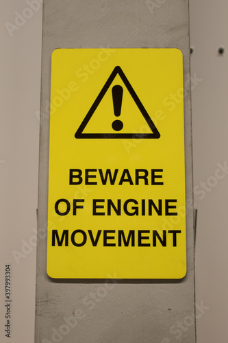 Beware of Engine Movement industrial sign with warning symbol on wall in yellow