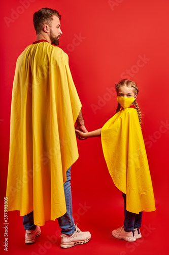 confident girl and man ready to fight against coronavirus, they stand in superhero costume, girl in medical mask, look at camera. isolated over red background