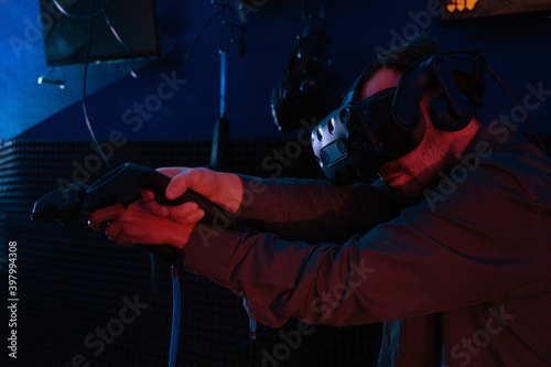 Man playing game using virtual reality headset and gamepads in dark room of playing club