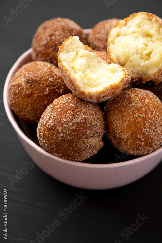 Homemade Fried Donut Holes in a pink bowl on a black surface, side view.
