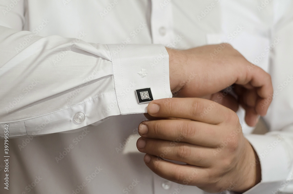 Groom's hands fasten the black cufflinks on his shirt, close-up. The preparations of the groom Groom's hands fasten the black cufflinks on his shirt, close-up. The preparations of the groom