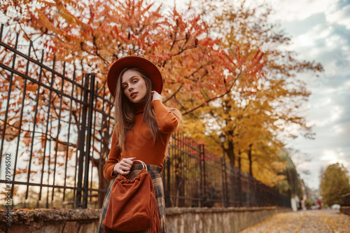 Young elegant  fashionable woman wearing stylish orange hat  turtleneck  holding suede handbag with fringe  posing in street. Outdoor autumn fashion portrait. Copy  empty space for text
