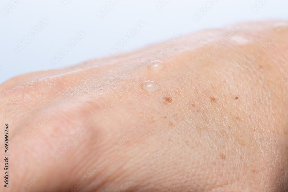 Fototapeta premium Water drops on woman hand skin, close up of wet human skin texture