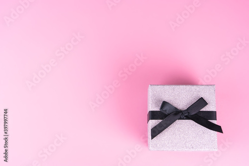 Small silver gift package with black bow, pink background, copy space
