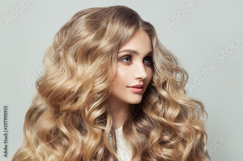 Portrait of beautiful young woman with long blonde curly hair on white