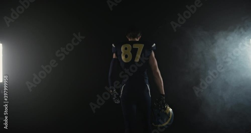 Tracking shot of of American football sportsman player walking with helmet in hand