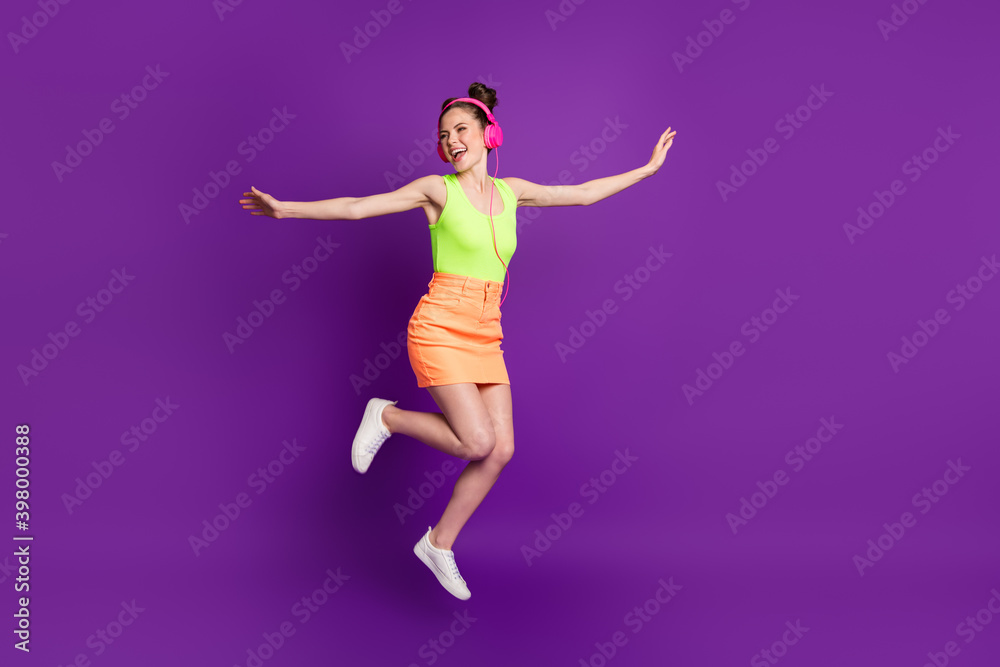 Full length body size view of attractive fit free carefree careless cheerful girl jumping listening melody isolated on bright violet color background