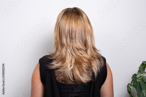 Rear view of a woman with long wavy blonde hair wear black sweater looking white background