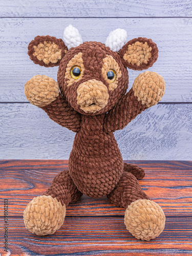 Plush bull toy on a wooden background. Soft toy with raised legs. Symbol of 2021 New Year.