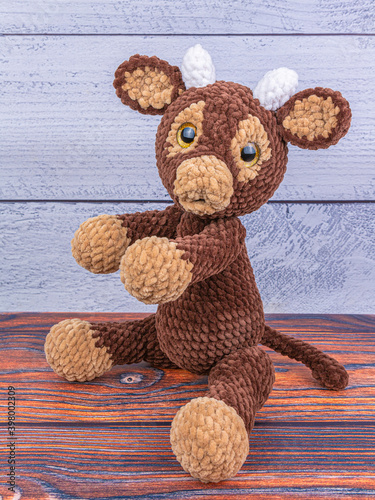 Plush bull toy on a wooden background. The soft toy stretches with its legs forward. Symbol of 2021 New Year.