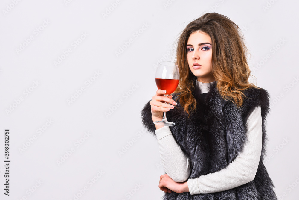 Fashion model long hair fur coat or vest hold wineglass. Girl enjoy luxury lifestyle attributes. Woman drink wine wear luxury fur clothing. Luxury winery concept. Fashionable lady likes luxury