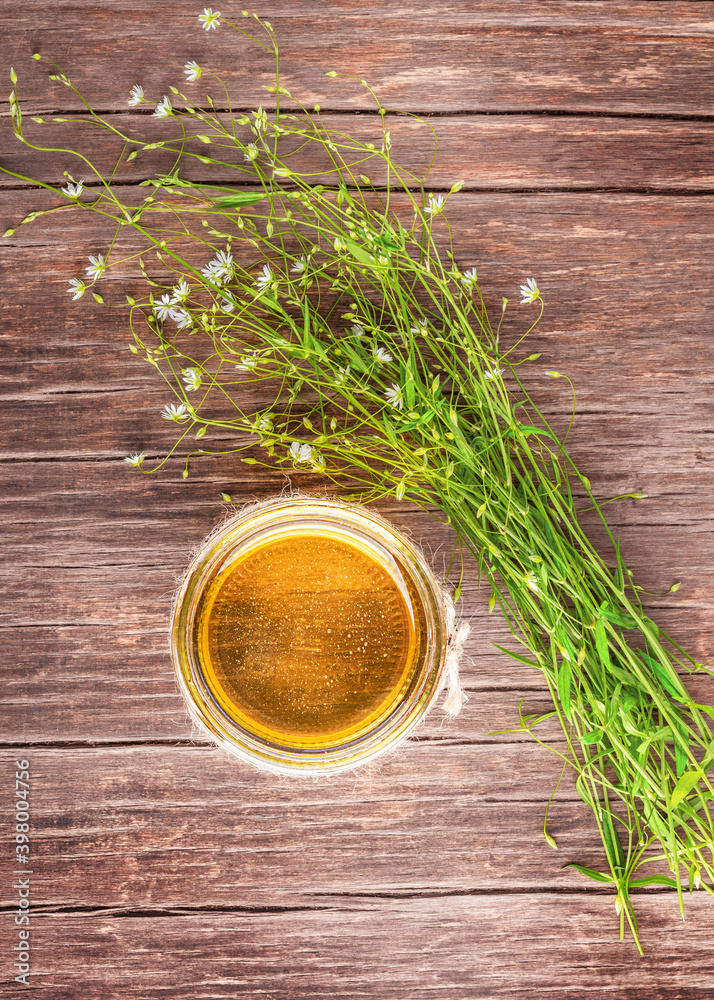 Honey in a glass jar and a bouquet of delicate wildflowers on a wooden brown background. Top view. Copy space.