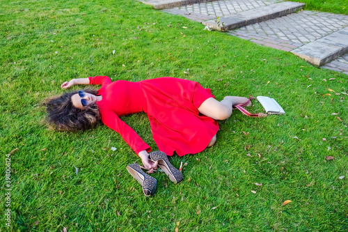 Relaxed young person teenage girl lying in grass. Teen girl brunette in red dress with a drink problem laying on the grass