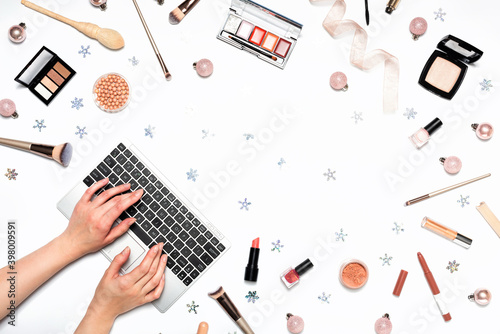 Female hands typing on laptop keyboard. Decorative cosmetics and makeup tools on white background with Christmas fir tree ornaments. Online shopping concept. Frame composition with copy space