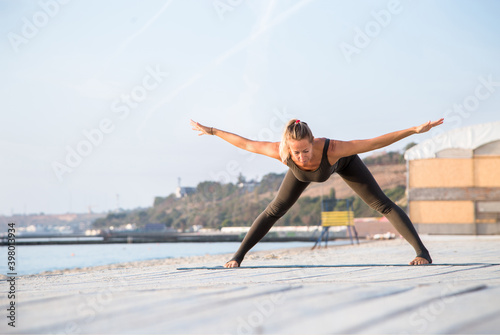 middle-aged female doing yoga asana on one leg on the sunny beach at plank f