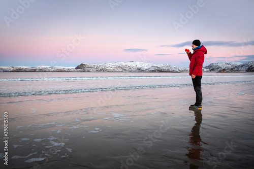 A man on the seashore drinks tea and admires the seascape. Pink sunset.