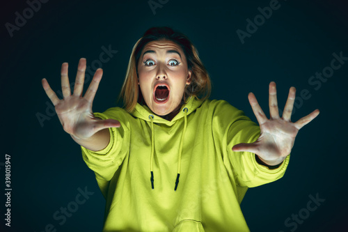 Pushing away. Portrait of young crazy scared and shocked caucasian woman isolated on dark background. Copyspace for ad. Bright facial expression, human emotions concept. Looking horror on TV, cinema. photo