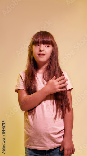 Portrait of disabled girl with Down syndrome looking aside while posing isolated over creative yellow background