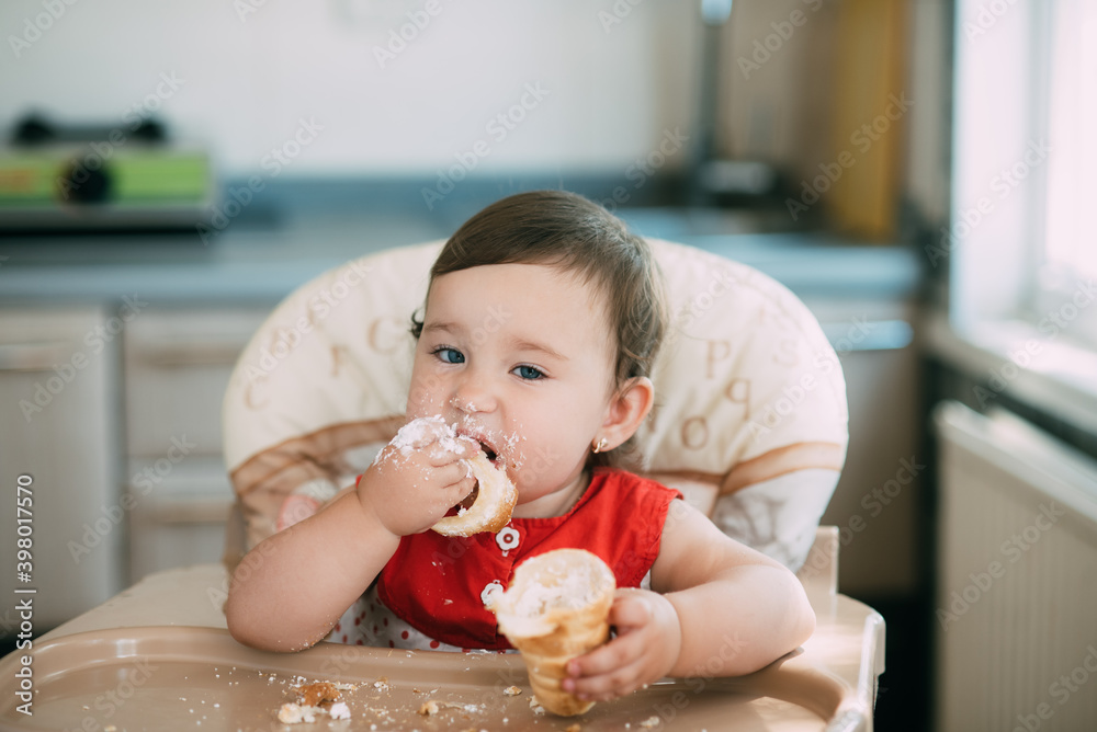 baby girl in the kitchen eating tubes with custard or protein cream baby girl in the kitchen eating tubes with custard or protein cream