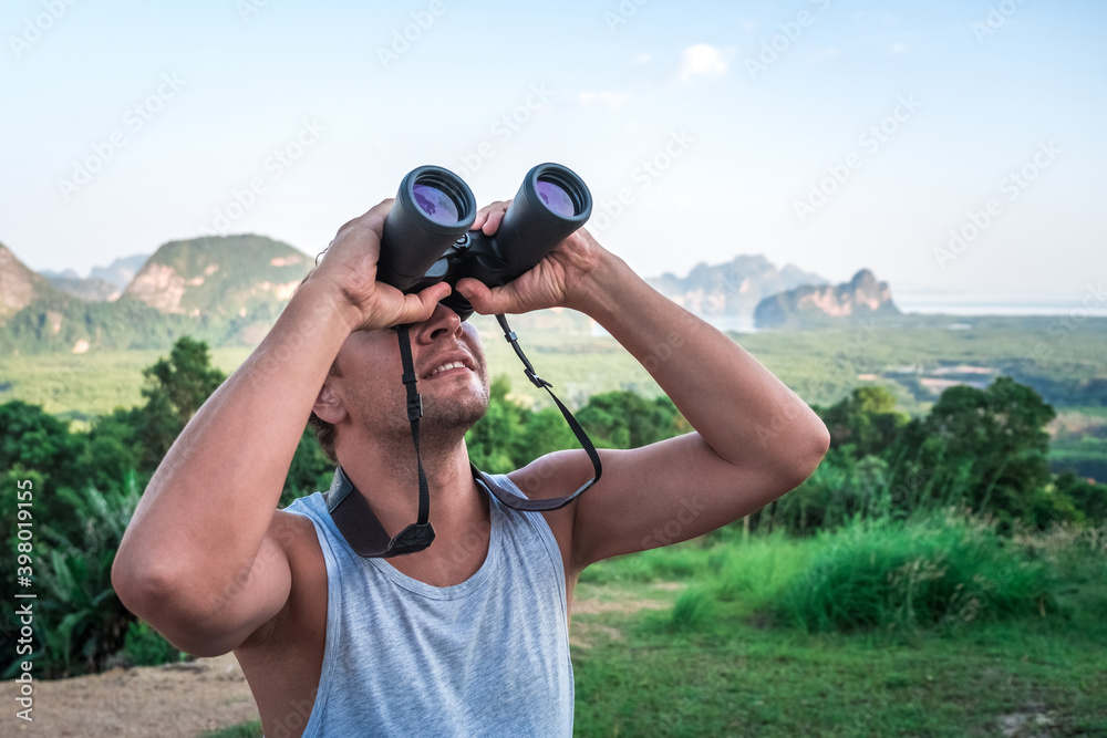 A young man looks into the sky through binoculars. A traveler on the background of wild nature