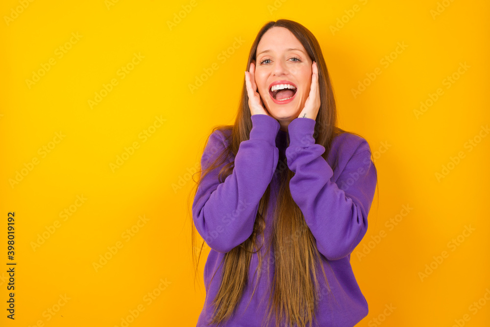 Young beautiful Caucasian woman wearing purple sweater against yellow wall Pleasant looking cheerful, Happy reaction