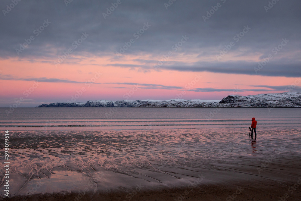 A photographer at the seaside takes a photo using a tripod. Seascape, pink dawn.