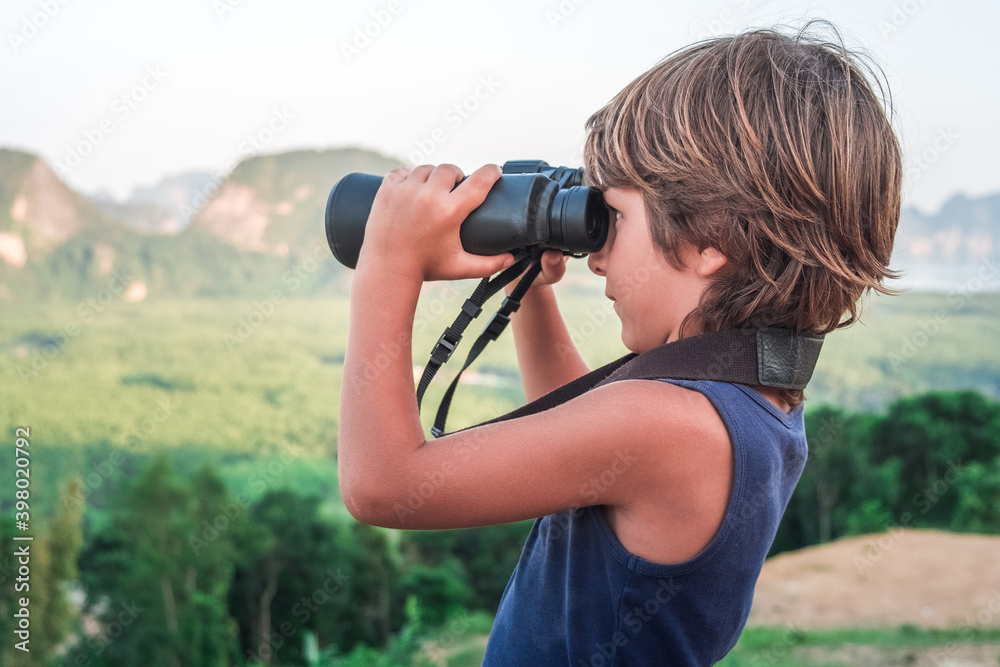 A little boy in a dark T-shirt from the top looks into the distance through binoculars at the wildlife