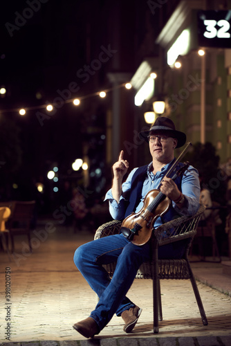 Portrait of a street musician man in a hat with a violin in the night city.