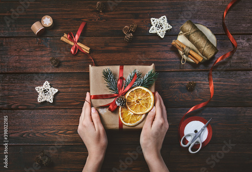 Hands of woman holding christmas gift box on wooden background. Presents wrapping inspirations. Packing process christmas gifts