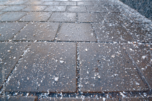 Rock salt crystal sprinkled on paving slabs to avoid slippery surface. Spreading rock salt, keeping sidewalks slip-free all season long. Spread de-icing reagents on sidewalk for melting ice and snow photo