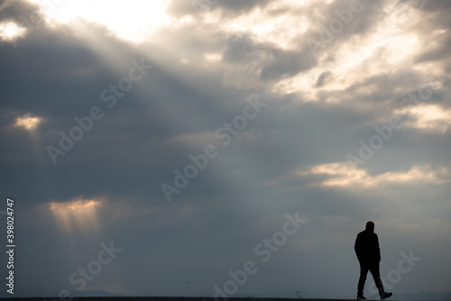 rayons de soleil trouant un ciel nuageux, dont un large et en diagonale tombant sur la silhouette d'un homme en train de marcher en bas de l'image  © Christophe