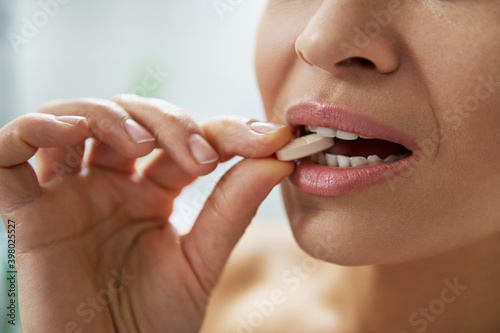 Close-up  woman puts a multivitamin pill in her mouth