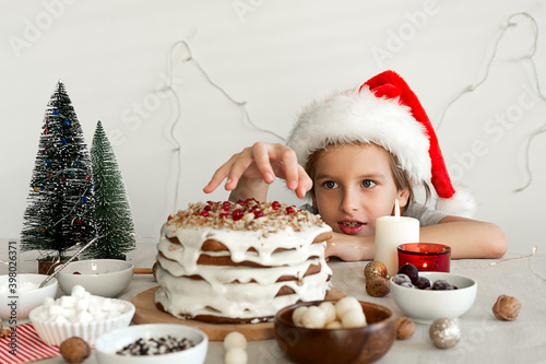 Preparing food for Christmas dinner. A boy in a red Santa hat wants to steal a piece of Christmas cake
