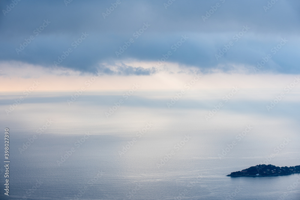 fond gris bleu et rose pâle représentant un ciel nuageux et une mer calme et plate en vue aérienne et le bout d'une péninsule en bas à droite de l'image 