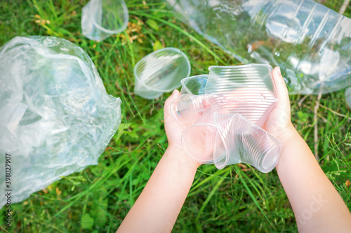Child s hands clean the park from used plastic utensils in the grass