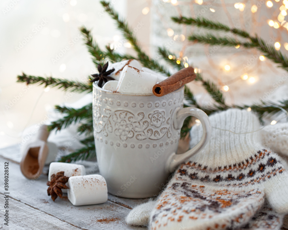 Winter hot drink. Cozy home composition with white mug with chocolate and marshmallow, cinnamon. Knitted mittens, christmas lights, wooden background. Festive holiday atmosphere, family spirit. Close Winter hot drink. Cozy home composition with white mug with chocolate and marshmallow, cinnamon. Knitted mittens, christmas lights, wooden background. Festive holiday atmosphere, family spirit. Close