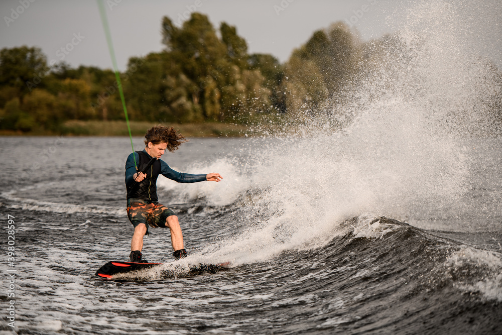 young athletic man holding taut rope and rides down on wave on wakeboard young athletic man holding taut rope and rides down on wave on wakeboard