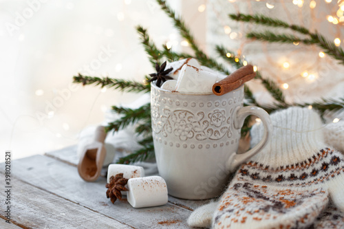 Winter hot drink. Cozy home composition with white mug with chocolate and marshmallow, cinnamon. Knitted mittens, christmas lights, wooden background. Festive holiday atmosphere, family spirit. Close