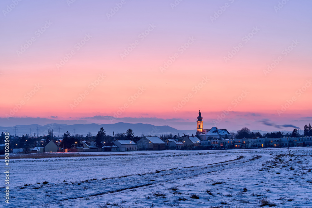 Illuminated church behind a snow covered field after sunset
