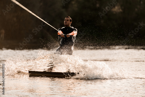 man in wetsuit is engaged in extreme water sports and rides on wakeboard