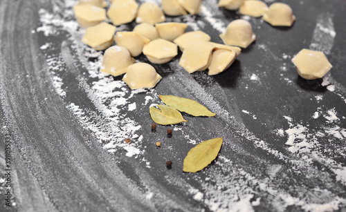 The background is a black table, sprinkled with flour, smeared by hand, on it are dumplings, in the center are bay leaves and peppercorns.